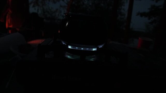 Camping kettle heating on a portable gas burner at night in an outdoor campsite setting