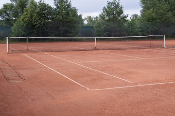 Fototapeta premium Empty clay tennis court with professional net and marked playing surface prepared for training sessions, matches and outdoor sports activities.