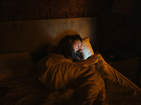 Woman lying awake in bed with smartphone 