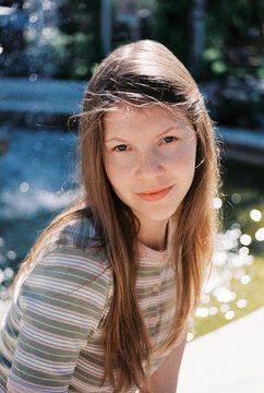 A young woman with freckles smiles softly in dappled sunlight