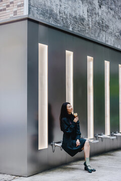 Woman Sitting Against Modern Architectural Wall Holding Coffee