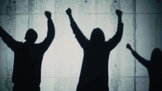 Shadows of three people raising hands in celebration against concrete wall