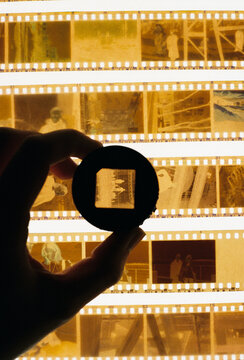 Hand holding a magnifying loupe over illuminated 35mm film negatives