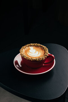 Red cup pistachio cappuccino with latte art on dark table