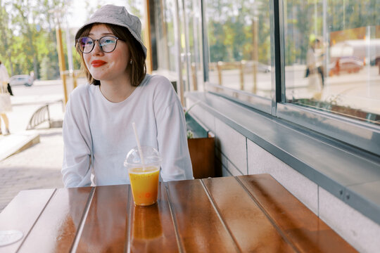 Young Woman Sits at a Table With a Drink in a City Street