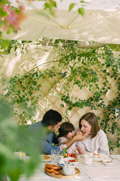 Father and mother with a toddler having breakfast in the garden