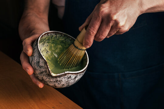 Hands whisking matcha tea in ceramic bowl at home