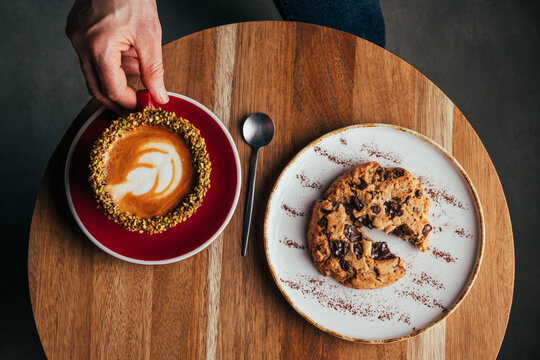 Overhead pistachio coffee with latte art and chocolate cookie on table