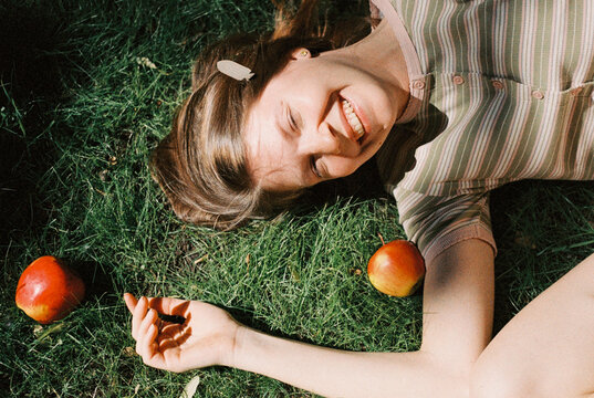 A woman laughs lying in the grass with fallen apples