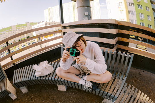 Young Person Sitting on Bench and Taking Photos in City