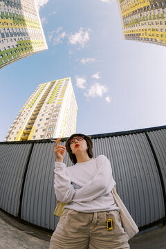 Young Woman Stands by Buildings and Holds a Cigarette in City