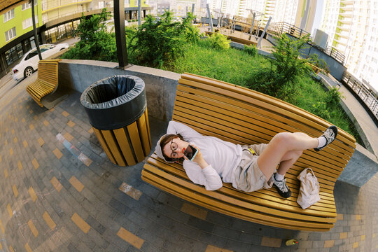 Person Lies on Bench While Using Phone in City Park