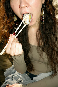Woman eating sushi with chopsticks on a wooden deck