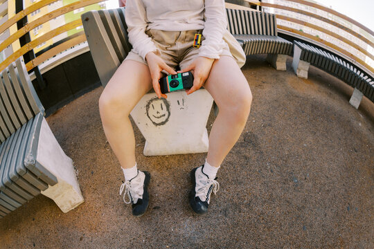 Person Sits on Bench Holding Camera in Urban Space During Daylight
