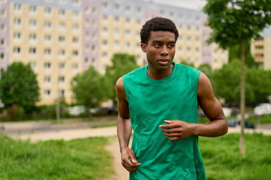 Runner Jogging in a Green Shirt Near Apartment Buildings in Summer
