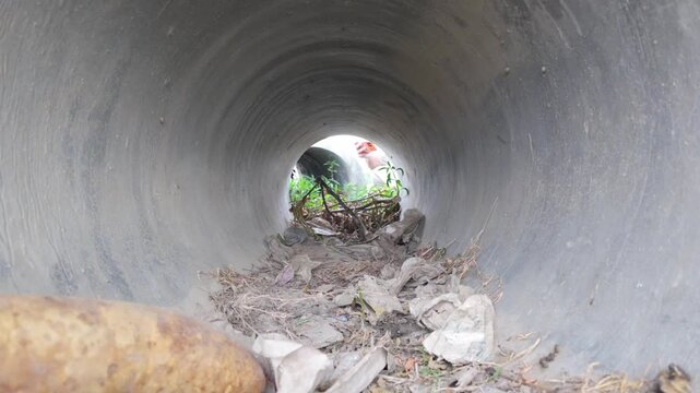 Large circular concrete culvert pipe with young man checking inside from opposite side.