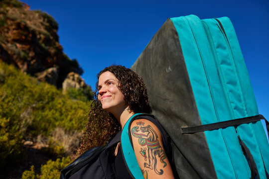 Rock climber carries crash pad in desert landscape during daytim