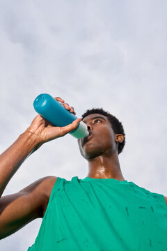 Young Man Drinks From a Blue Sports Bottle in Daylight
