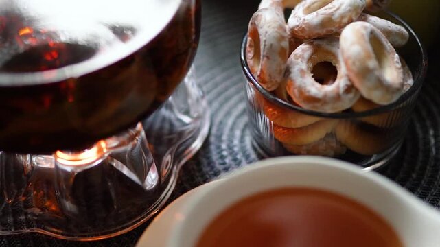 Cozy evening tea served in a glass teapot with fresh bagels and cookies on a rustic table. Warm candlelight creates a relaxing, homely atmosphere perfect for autumn or winter evenings