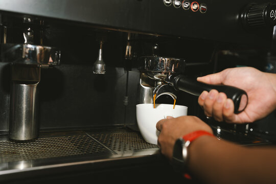 Barista pulling a fresh espresso shot into a white cup using a professional coffee machine in a modern specialty coffee shop.