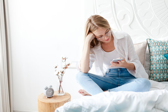 Young woman using smartphone in bed at home. Girl relaxing with mobile phone, learning online, shopping, doomscrolling. Digital lifestyle, communication, connection