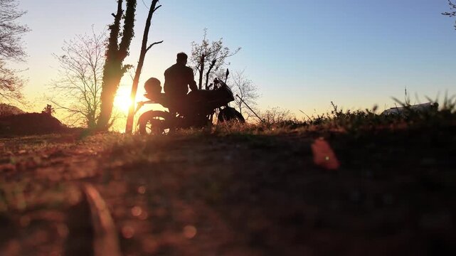 A steady, low-angle shot capturing the dramatic shadow of a motorcyclist cast on the ground during a vibrant golden hour sunset. A moody and artistic scene highlighting adventure and travel themes.