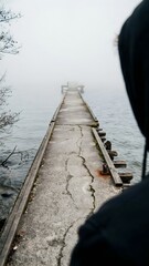 Fototapeta premium Lonely Dock Extending into Misty Water with Overcast Sky and Bare Tree Branches