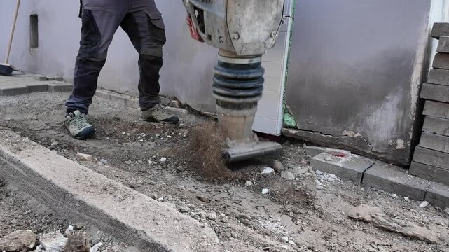 Construction worker compacting soil with a vibratory tamper near a building