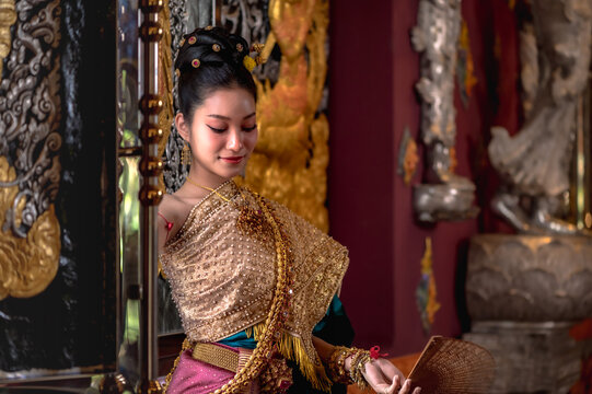 Thai woman in traditional Royal Chakraphat dress and golden jewelry posing gracefully inside ancient temple vihara