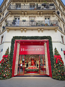 Paris, France - December 10, 2025: the storefront of Histoire d'Or decorated for the winter holidays. Christmas trees flank the entrance, while classic Parisian architectural balconies extend above