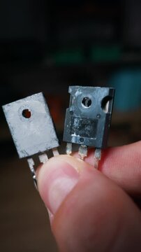 A close-up view of a hand holding two mosfet power transistors with one showing signs of wear. Concept of hardware repair, electrical engineering, semiconductor testing, and diy electronics.