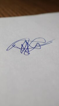 Close-up view of an orange ballpoint pen tip touching a blank sheet of white paper on a wooden desk. Concept of creativity, signing a contract, journaling, and academic preparation.