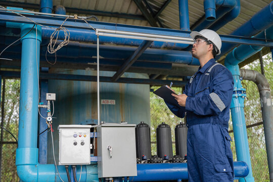 Professional engineer performing maintenance inspection of industrial water filtration system with multiple membrane units. Technician recording operational data for water treatment facility process.