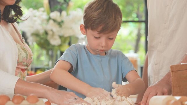 Parents and their son kneading and rolling bread dough in a sunlit kitchen