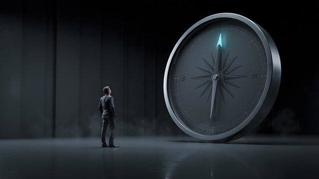A businessman in a suit standing in a dark room looking at a giant glowing compass navigation tool representing direction and strategic planning