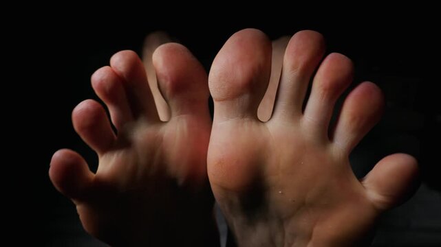 Bare human toes and feet spread wide against a solid black background with low-key lighting highlighting skin textures. Concept of anatomy, skin health, podiatry, and personal hygiene.