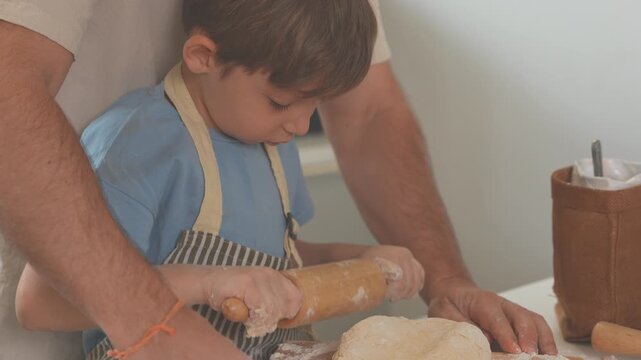 Mother and father helping their son knead bread dough in a sunlit kitchen