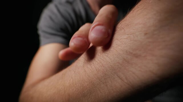 A close-up view shows a Caucasian man pointing his finger at the visible hair on his forearm in a studio setting. Concept of masculinity, body grooming, skin texture, and anatomy.