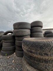Obraz premium Pile of used tires and second hand car tyres. Old black rubber tyre waste for recycle, landfill or sale at manufacturing yard background for automotive industry and environmental concept.