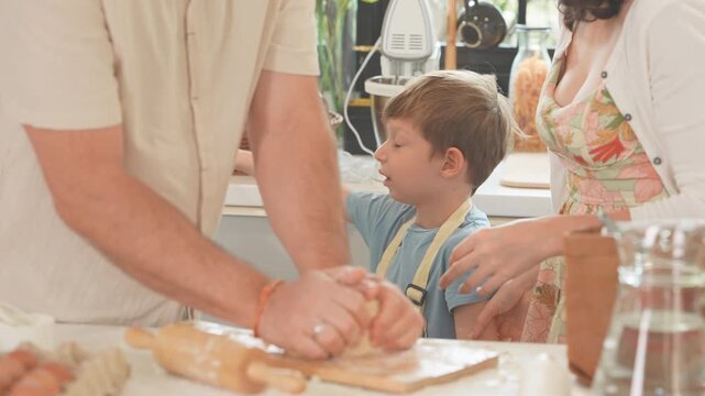 Little boy learning to bake bread with his mum and dad in a sunlit kitchen