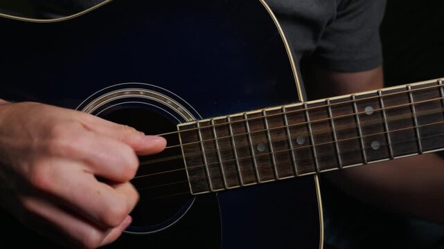 A close-up view of a musician hand strumming a dark blue acoustic guitar with precision. The shallow depth of field highlights the wooden texture and the vibration of the strings.