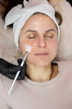 Hydrating cosmetology. Face nourishing. Beauty master hand in gloves applying moisturizing product for woman with brush in professional spa.