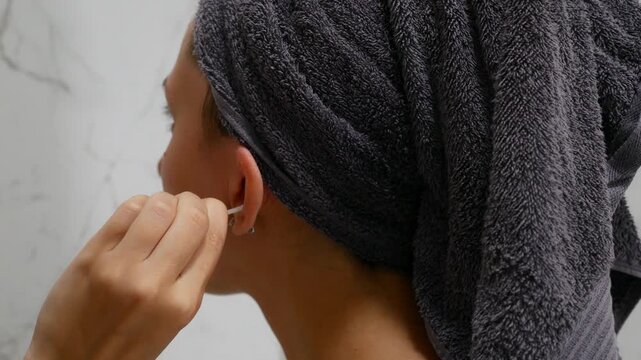 Woman cleaning outer ear with cotton swab during daily personal hygiene routine.
