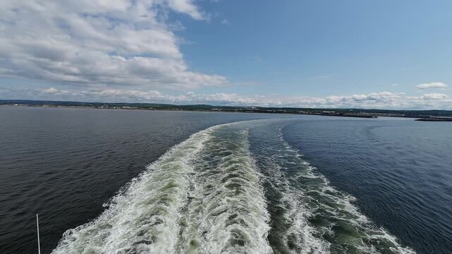 Dynamic wake patterns form behind a departing ferry as it leaves Matane Harbor.