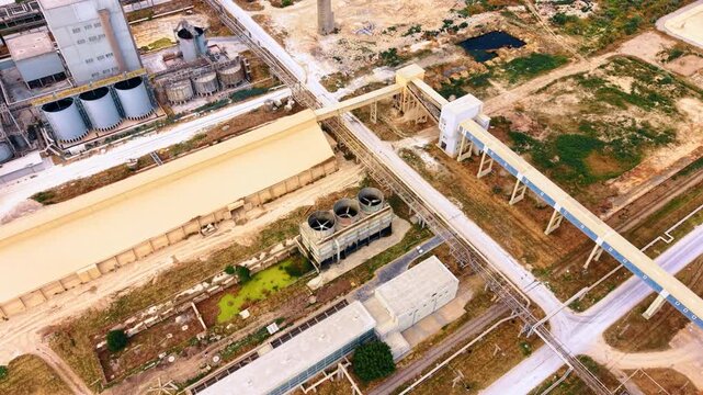 Factory cooling units and conveyors across processing complex. Elevated view includes storage vessels, utility buildings, railway tracks and green wastewater ponds.