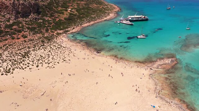 Aerial drone view of Balos beach with visitors on the white sand and boats moored offshore, Balos, Greece