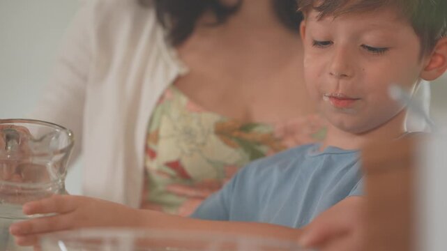 Little boy tasting batter while cooking with his mother at the kitchen counter