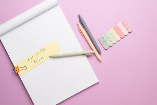 A note pad with blank grid paper on a bright purple background with multicolored sticky note tabs and pastel pens. Written out of the office message.