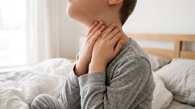 Young boy touching his painful throat in bedroom to indicate illness