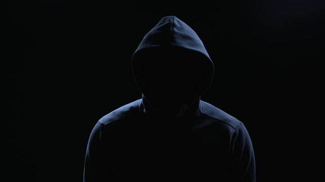 Silhouette of hooded man on black background, threatening villain